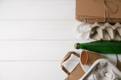 Photo of Heap of waste paper and glass bottle on white wooden table, flat lay. Space for text