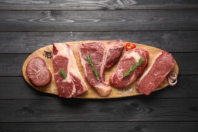 Pieces of raw beef meat and spices on black wooden table, top view