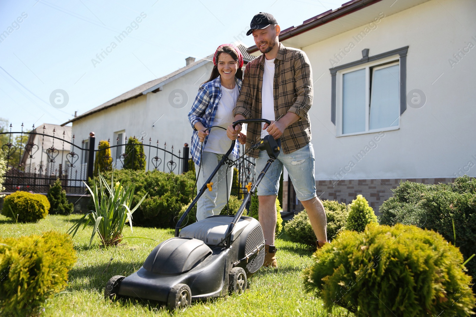 Photo of Happy couple spending time together while cutting green grass with lawn mower in garden