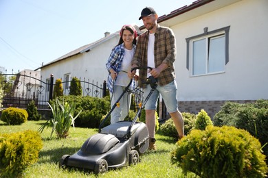 Happy couple spending time together while cutting green grass with lawn mower in garden