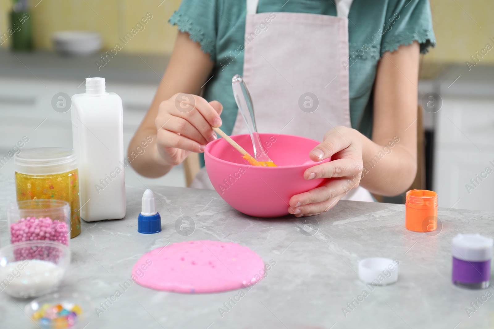 Photo of Little girl making homemade slime toy at table in kitchen, closeup
