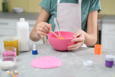 Little girl making homemade slime toy at table in kitchen, closeup