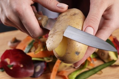 Woman peeling fresh potato with knife at table, closeup