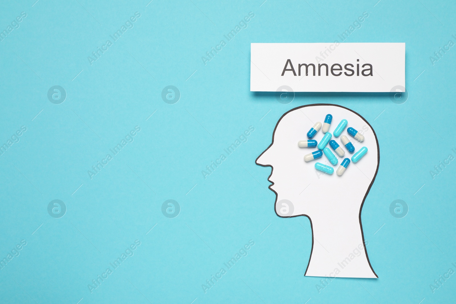 Photo of Human head cutout with pills as brain and word Amnesia on light blue background, flat lay. Space for text