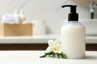 Photo of Dispenser of liquid soap and freesia flower on white table in bathroom, space for text