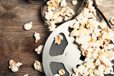 Tasty popcorn and film reel on wooden background, top view. Cinema snack