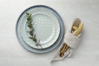 Photo of Stylish setting with cutlery, napkin, eucalyptus branch and plates on white table, top view