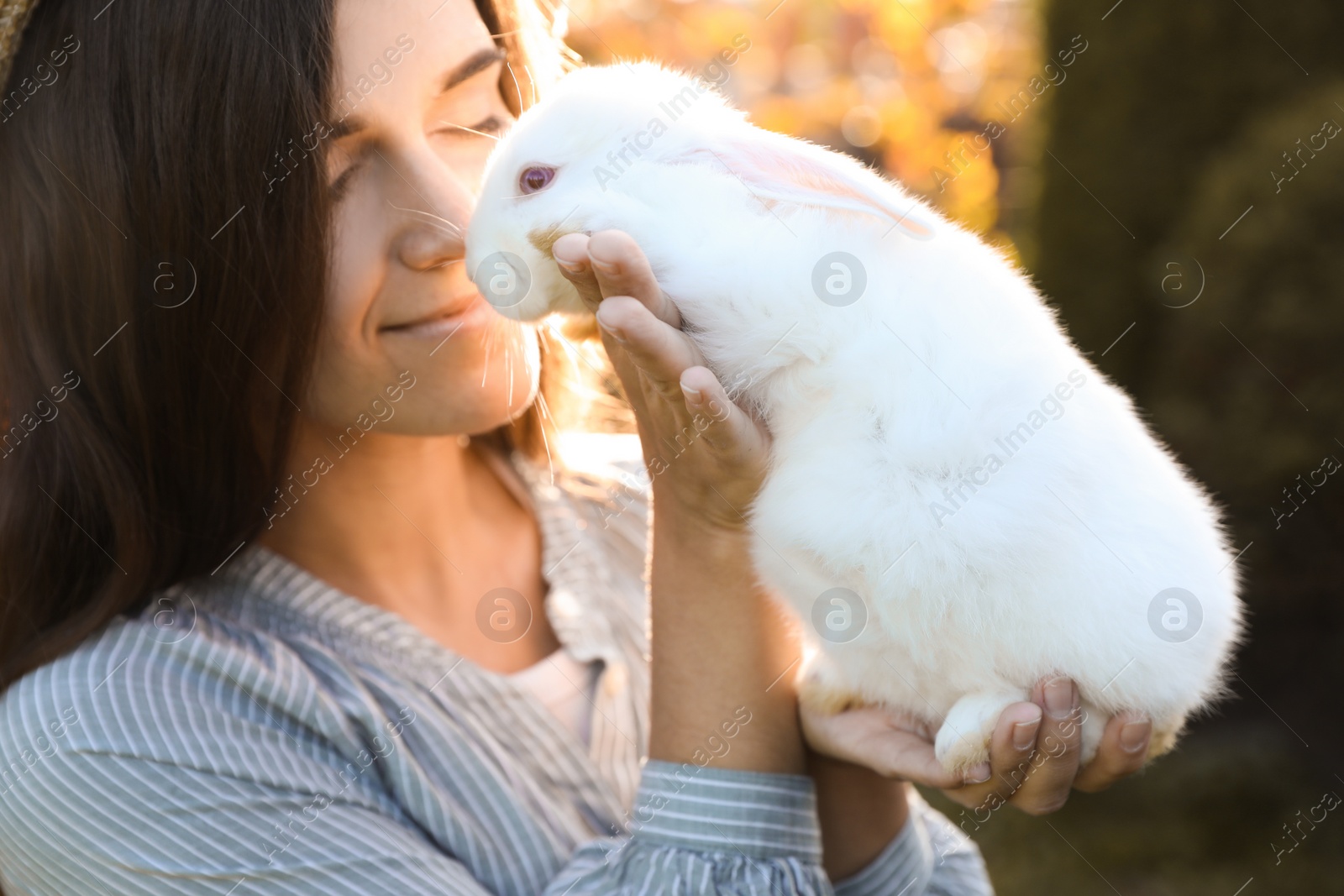 Photo of Happy woman holding cute rabbit outdoors on sunny day, closeup