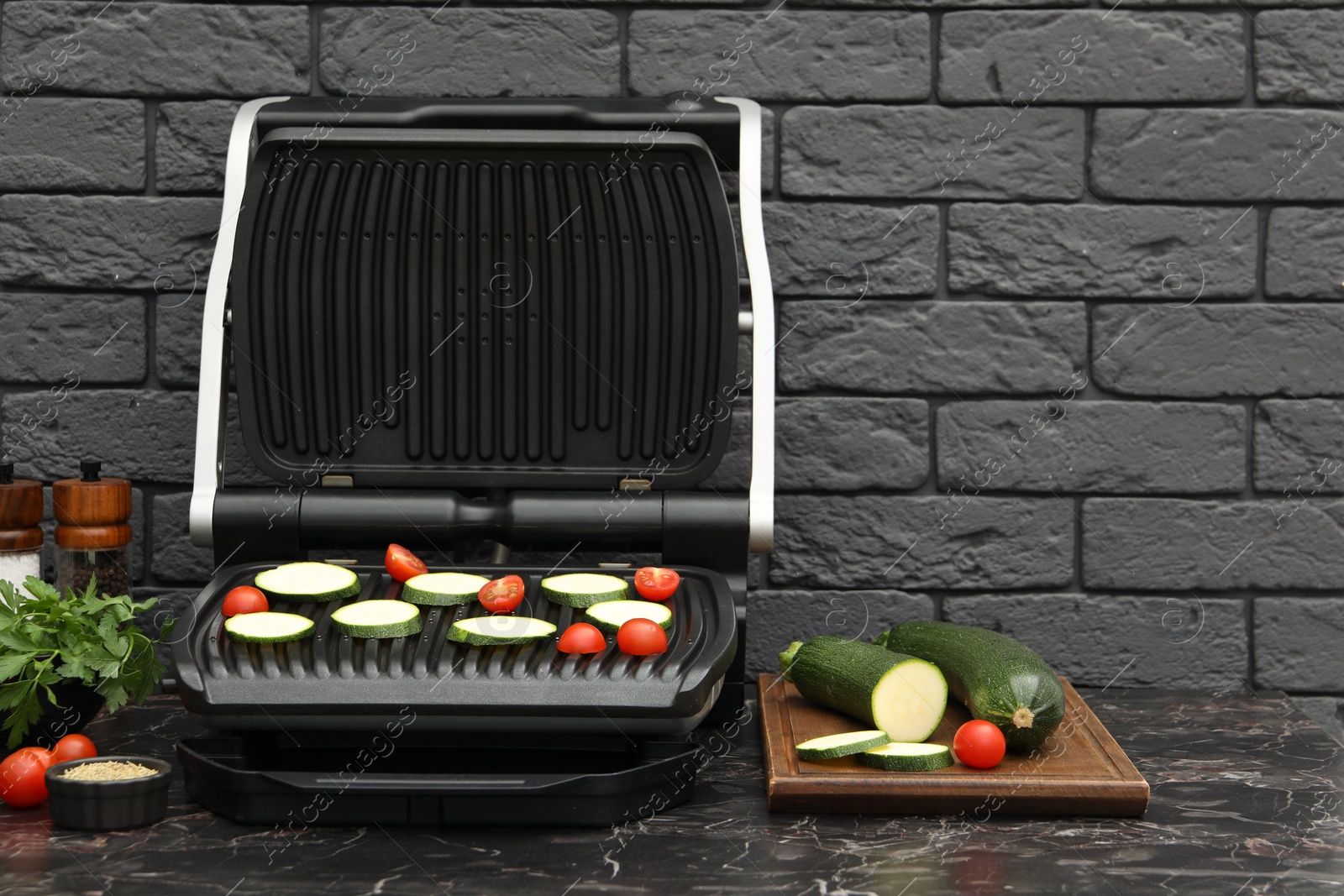 Photo of Electric grill with vegetables and spices on black marble table