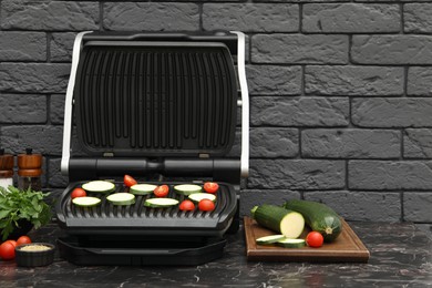 Photo of Electric grill with vegetables and spices on black marble table