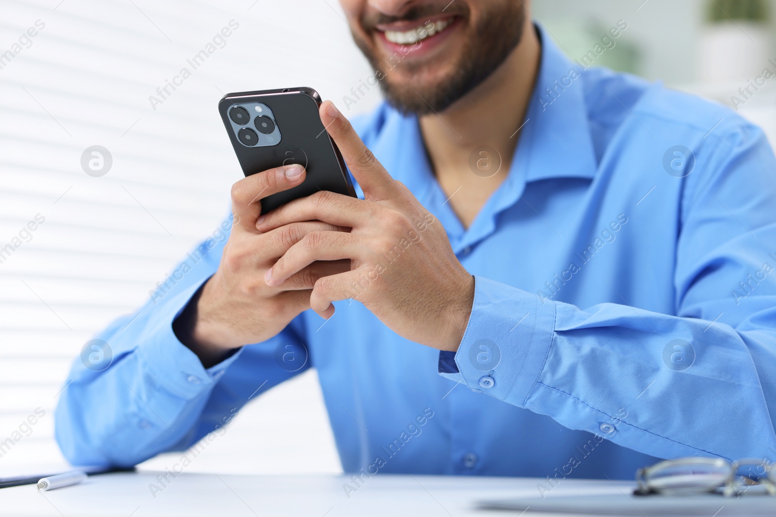 Photo of Man using smartphone at white table in office, closeup