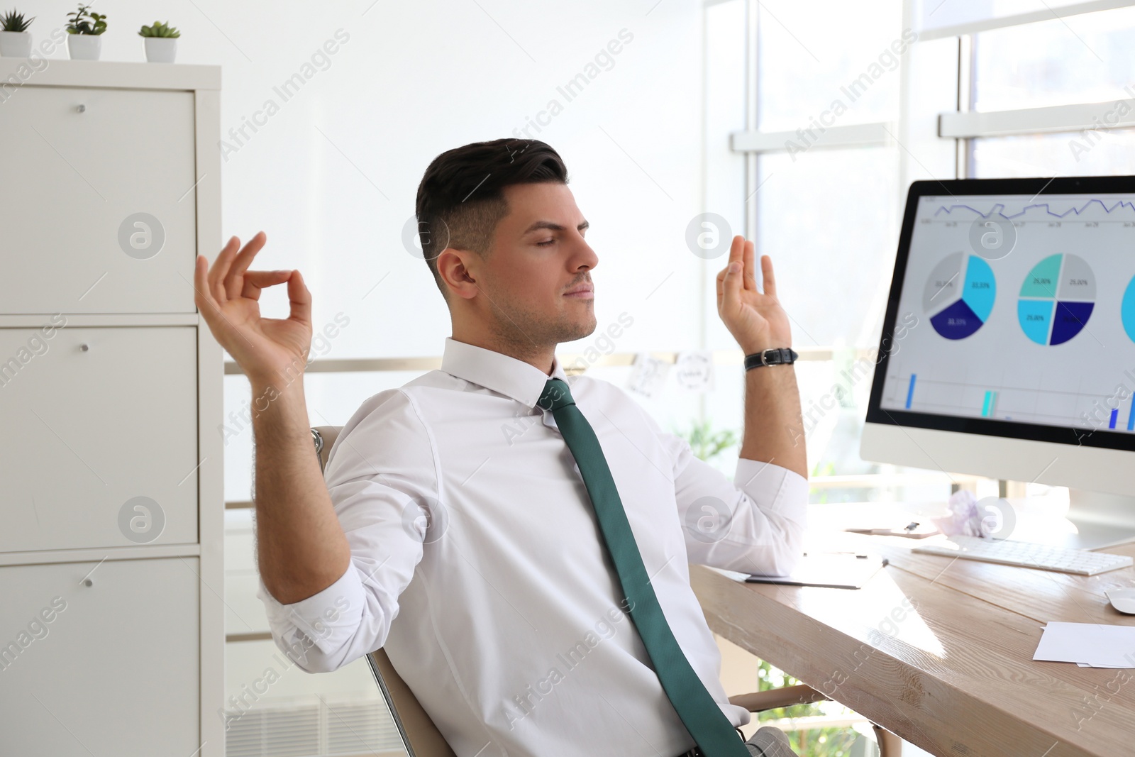 Photo of Businessman meditating at workplace in office. Stress relieving exercise