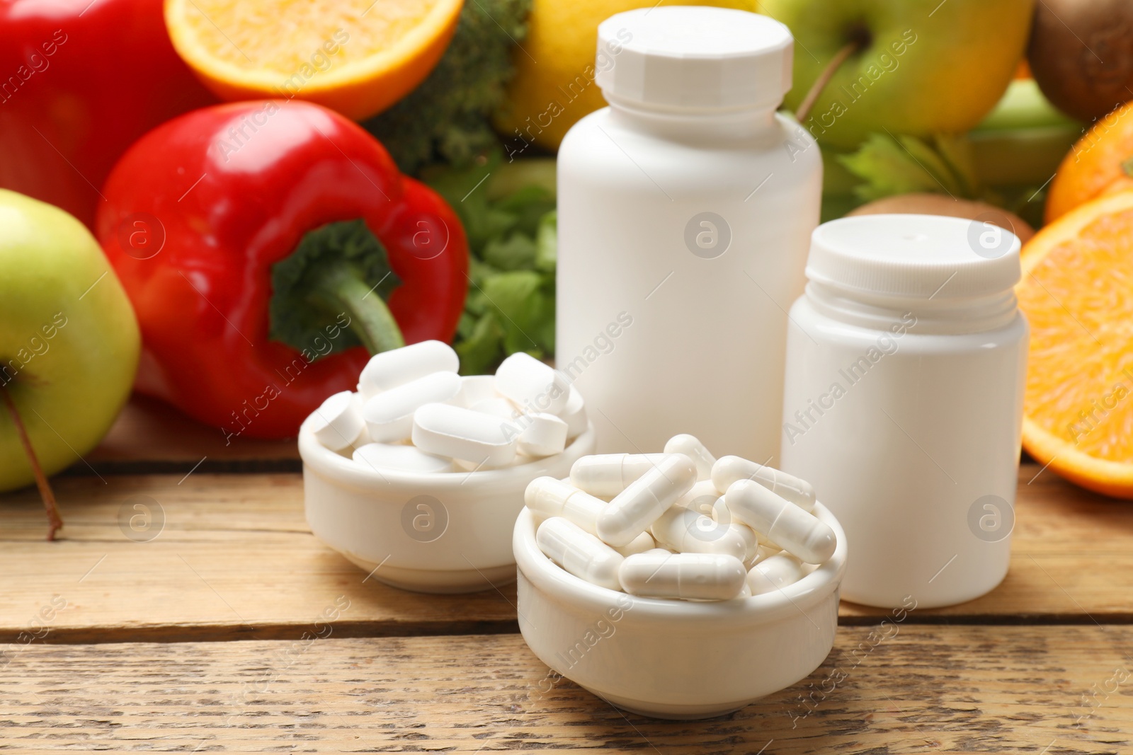 Photo of Dietary supplements. Plastic bottles, pills in bowls and food products on wooden table