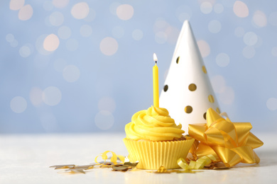 Delicious birthday cupcake with cream and burning candle on white table. Space for text