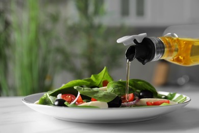 Photo of Pouring cooking oil onto plate with salad on white table, closeup