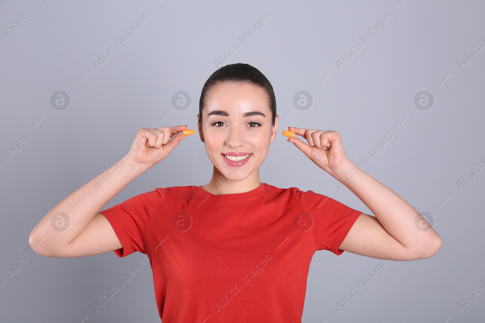 Photo of Young woman inserting foam ear plugs on grey background