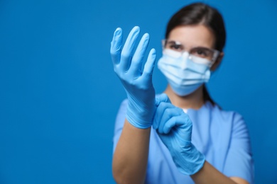 Photo of Doctor in protective mask and medical gloves against blue background, focus on hands. Space for text