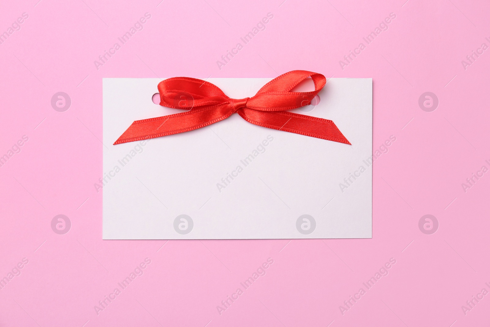 Photo of Blank gift tag with satin ribbon on color background, top view