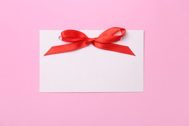 Photo of Blank gift tag with satin ribbon on color background, top view