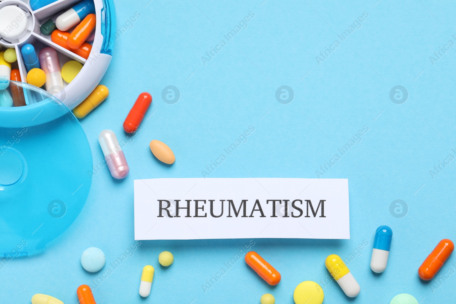 Photo of Card with word Rheumatism and pills on light blue background, flat lay. Space for text