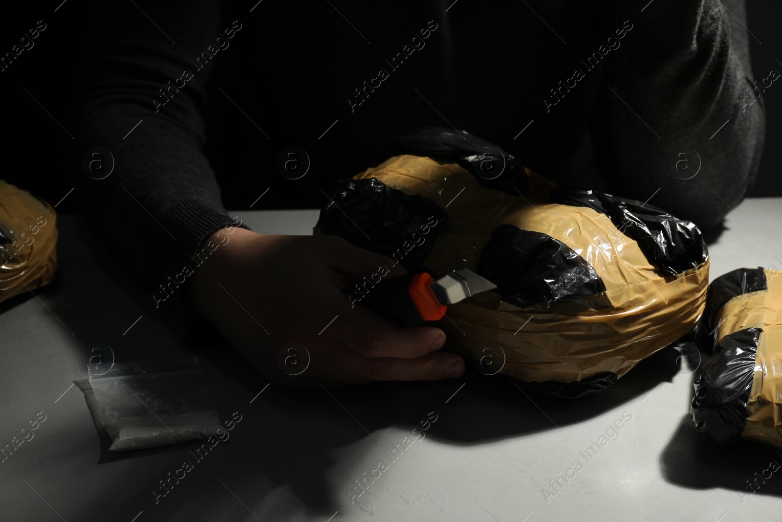 Photo of Smuggling and drug trafficking. Man opening package of narcotics with box cutter in darkness, closeup