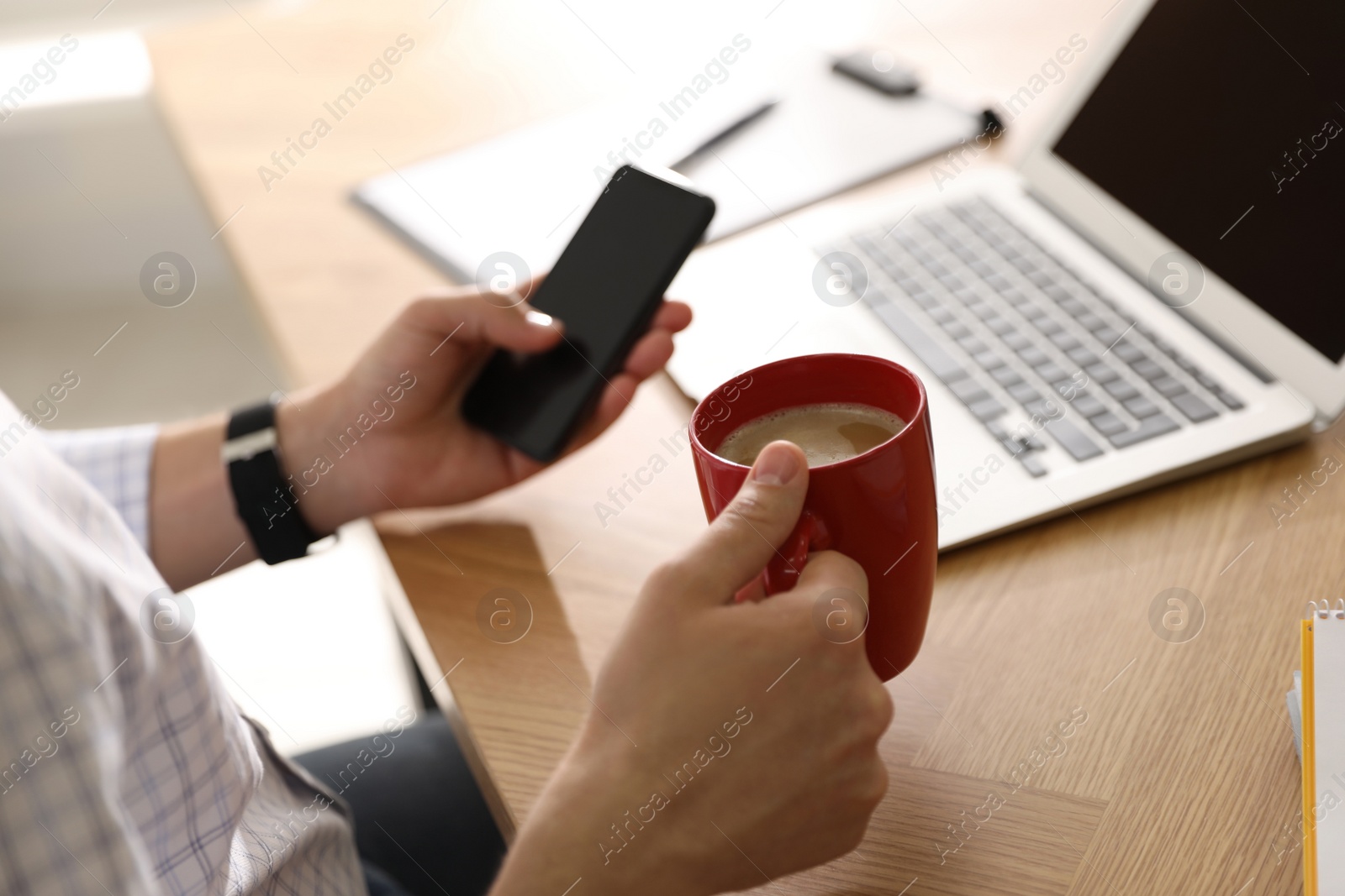 Photo of Man with cup of coffee and smartphone at workplace, closeup