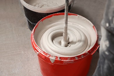 Photo of Mixing putty with electric mixer in red bucket indoors