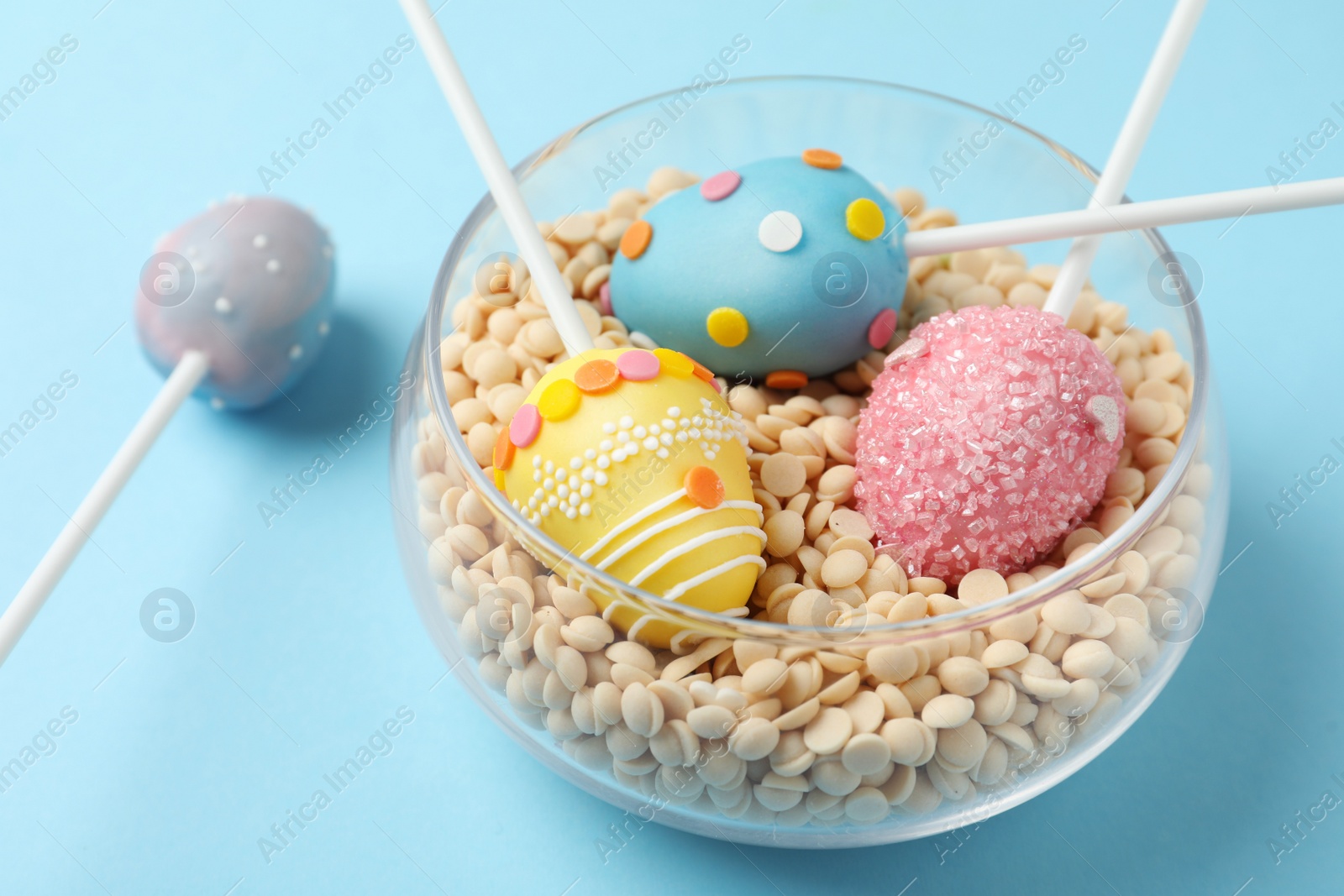 Photo of Egg shaped cake pops for Easter celebration on light blue background, closeup