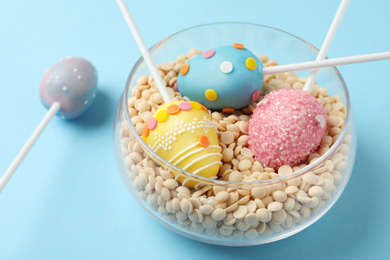 Egg shaped cake pops for Easter celebration on light blue background, closeup