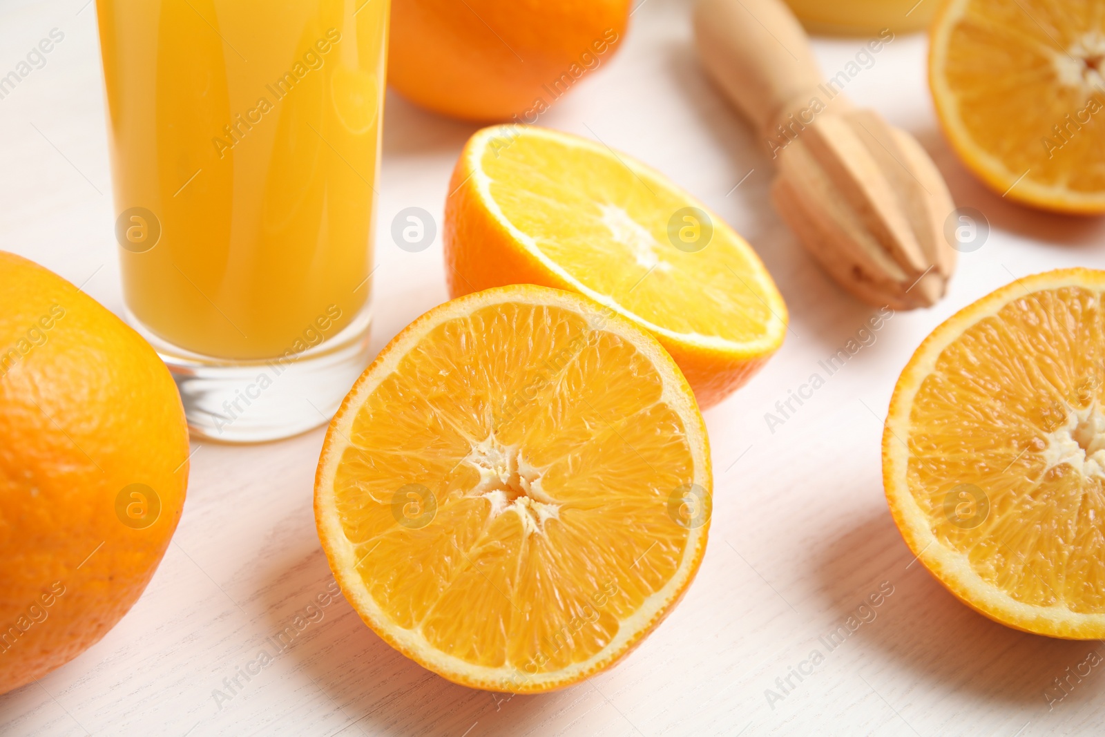 Photo of Fresh ripe oranges, juice and reamer on white wooden table