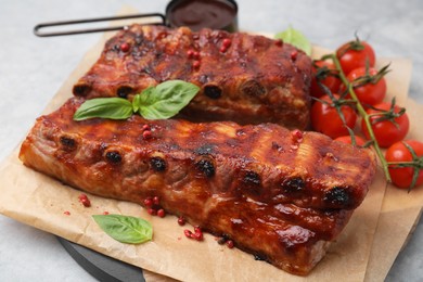 Photo of Tasty roasted pork ribs served with sauce, basil and tomatoes on grey table, closeup