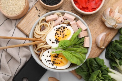 Photo of Bowl of delicious ramen with meat, egg and ingredients on table, flat lay. Noodle soup