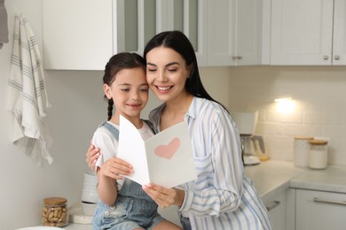 Little daughter congratulating her mom in kitchen at home. Happy Mother's Day