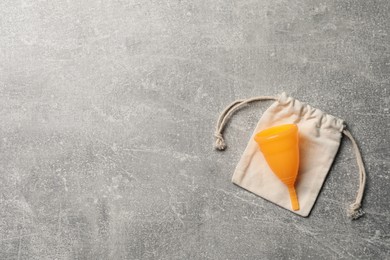 Photo of Menstrual cup and cotton bag on grey background, top view with space for text. Reusable feminine hygiene product