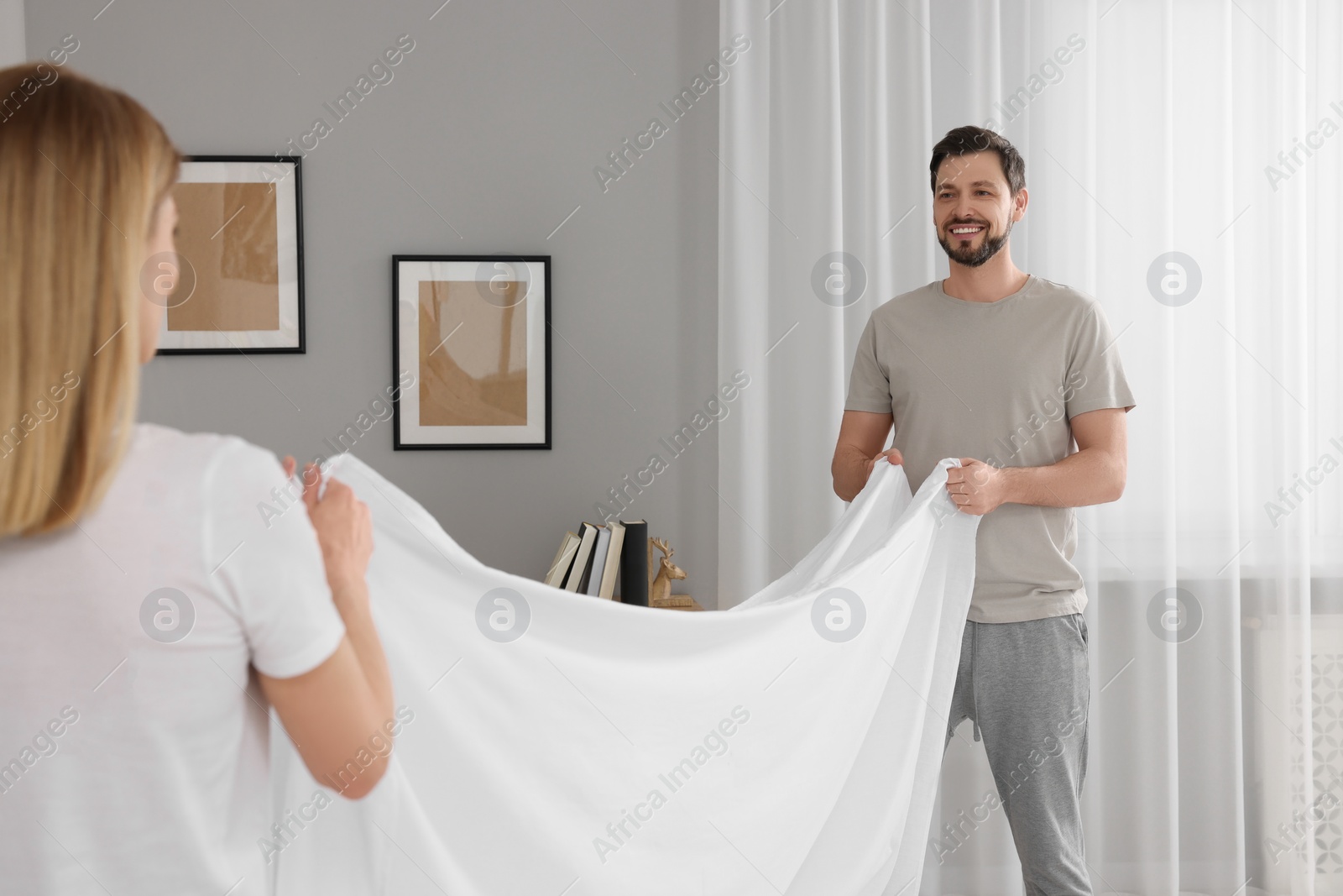 Photo of Couple changing bed linens in room. Domestic chores