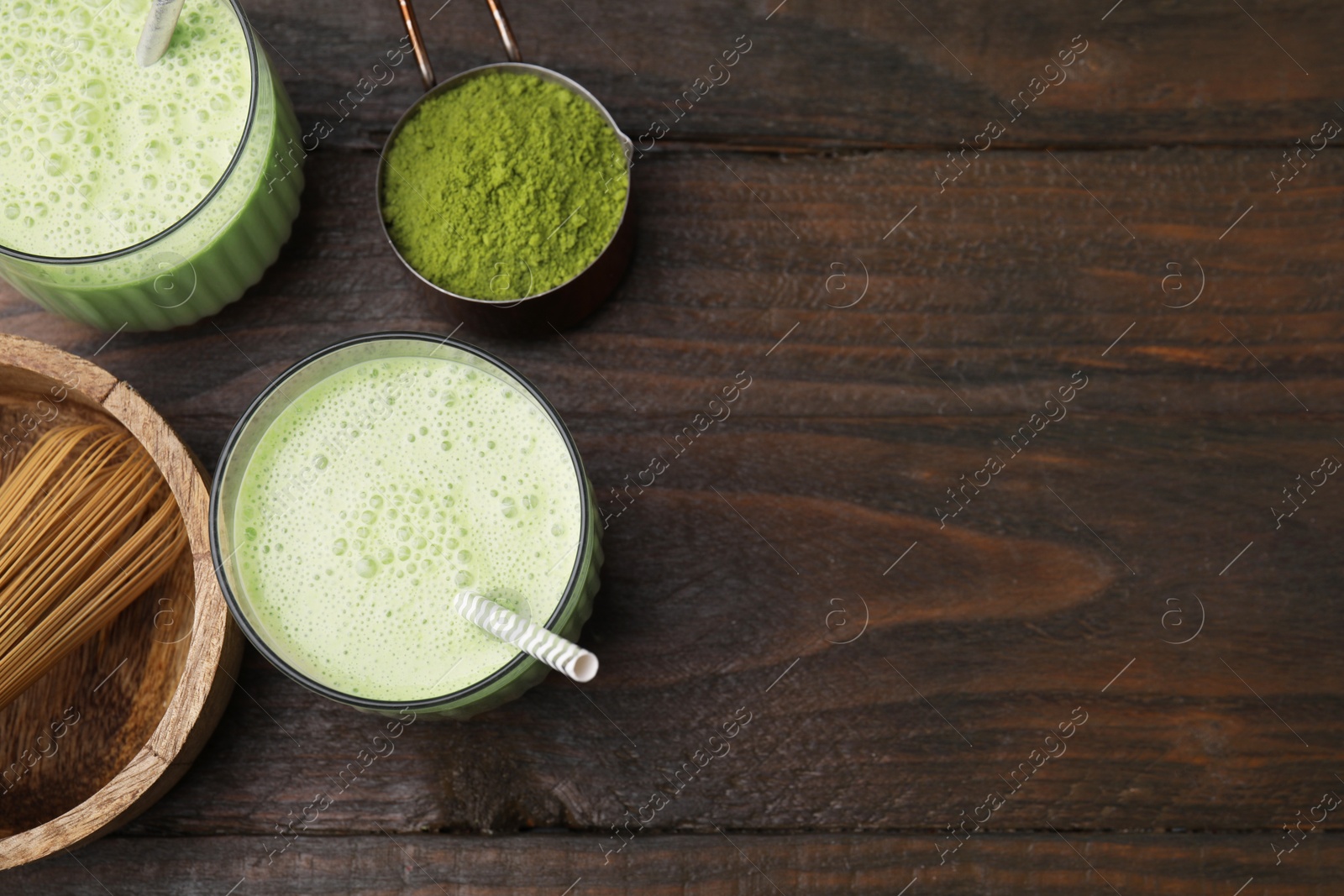 Photo of Tasty matcha smoothie, powder and bamboo whisk on wooden table, flat lay. Space for text