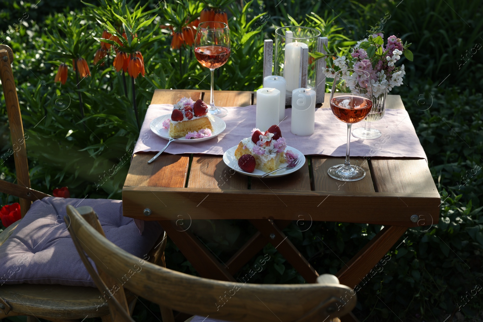Photo of Vase with spring flowers, wine and cake on table served for romantic date in garden