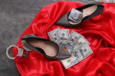 Photo of Prostitution concept. Handcuffs, panties, dollar banknotes, condoms and high heeled shoes on grey textured background, flat lay