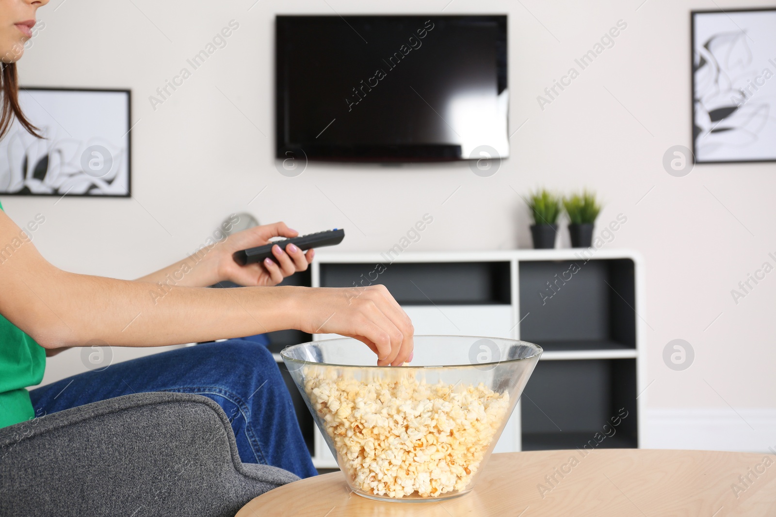 Photo of Young woman watching TV while eating popcorn at home