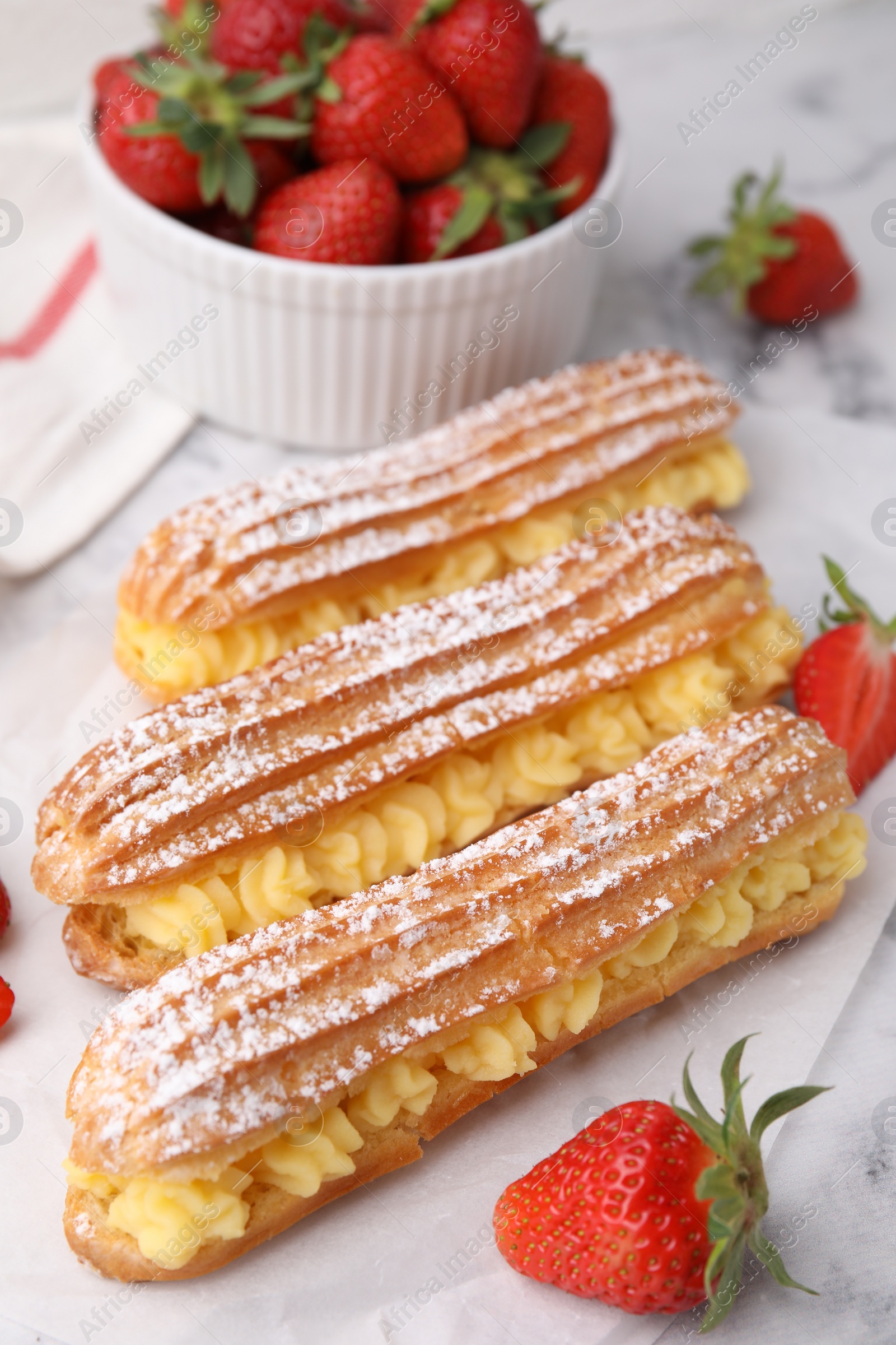 Photo of Delicious eclairs filled with cream and strawberries on table