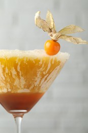 Delicious cocktail decorated with physalis fruit on blurred background, closeup