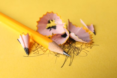 Photo of One sharp graphite pencil, scribbles and shavings on yellow background, closeup