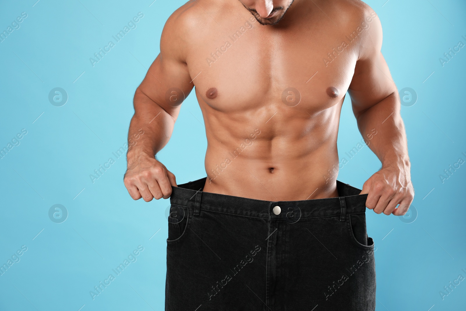 Photo of Young man with slim body in old big size jeans on light blue background, closeup view