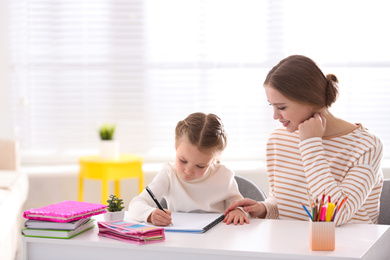 Woman helping her daughter with homework at table indoors