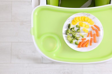 Photo of High chair with healthy baby food served on light green tray indoors, top view