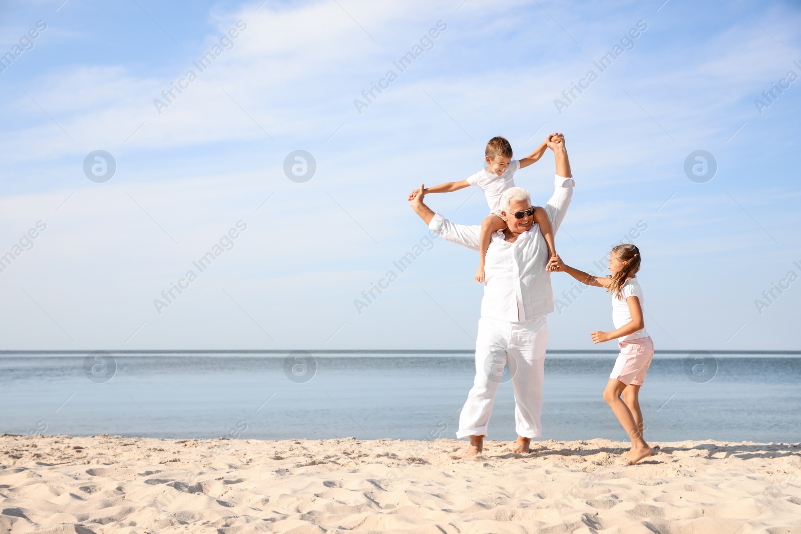 Photo of Cute little children with grandfather spending time together on sea beach