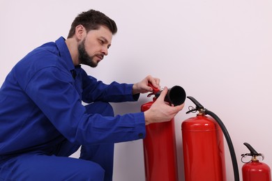 Man in uniform checking fire extinguishers indoors