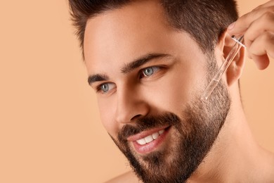 Handsome man applying cosmetic serum onto face on beige background, closeup