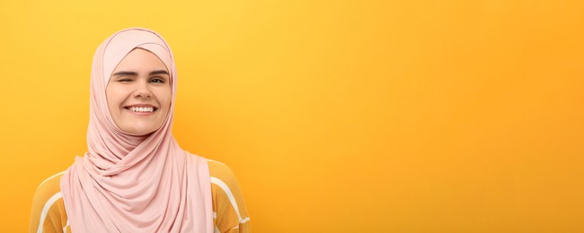 Portrait of Muslim woman in hijab winking on yellow background, space for text. Banner design