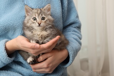 Photo of Woman holding cute fluffy kitten at home, closeup. Space for text